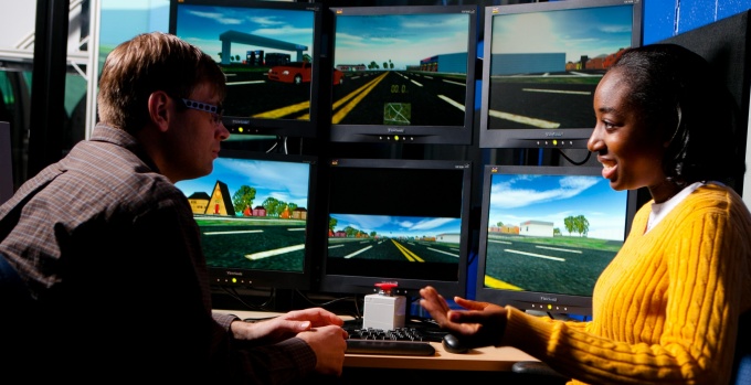 student Lesthia Isaacs and her professor talking in Furnas Lab. Computers in background with vehicle simulation. 